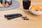A remote control without its cover and batteries is lying next to a bowl of crisps and a glass of dark red liquid on the table.