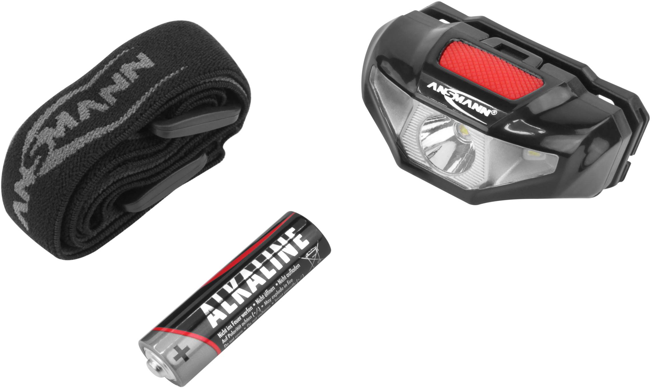 Black head torch with red button, battery compartment and elastic headband next to an alkaline battery.
