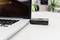 A laptop is sitting on a table. A small, black speaker or similar device is leaning against the right side of the laptop.