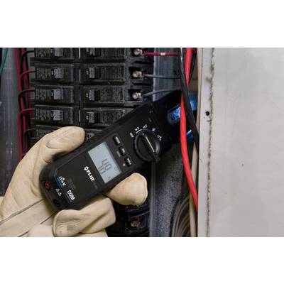 An electrician is using a digital multimeter to measure voltage at a fuse box. He is wearing protective gloves.