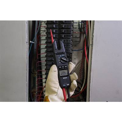 A person is holding a multimeter measuring a voltage of 120V at an open fuse box. Various cables are visible.