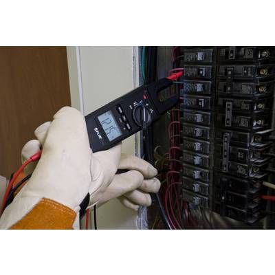 A person wearing protective gloves is conducting a voltage test in the fuse box using an electrical measuring device.