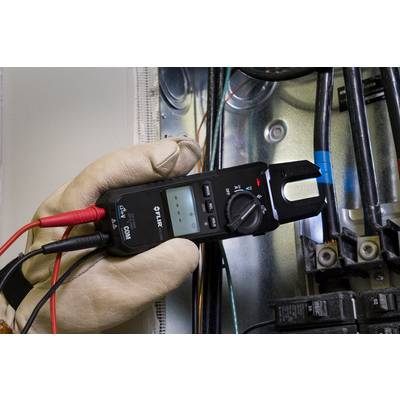 A hand in a glove holds an electrical measuring device over cables in a fuse box. The display is showing measurement data.