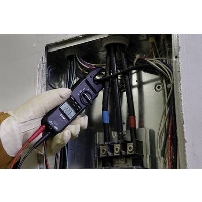 A person is checking the voltage of a fuse box with a multimeter; the display shows 222 volts.