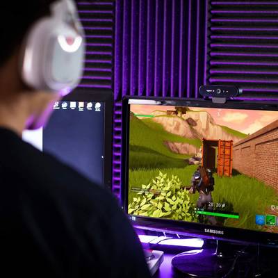 A person is playing a video game on a computer screen. The scene depicts a landscape with grass and a container.