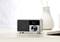 A white digital radio with a black screen displays 'Kaffen' and 'Time to Chill'. It sits on a table next to a book and a vase.
