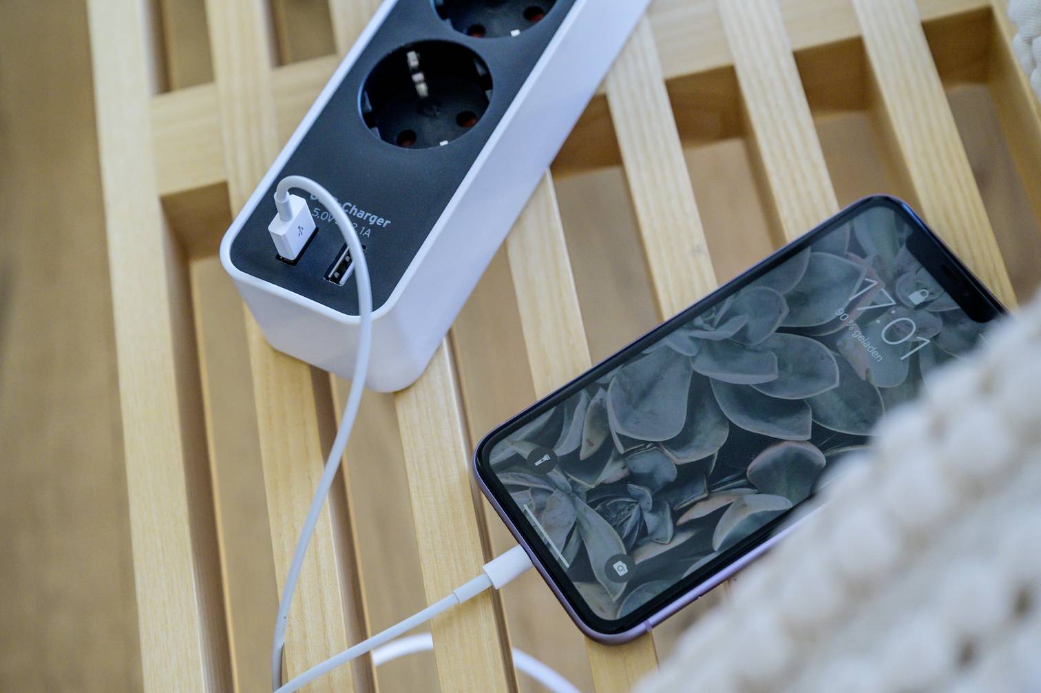 A smartphone is being charged with a USB cable at a multi-socket extension lead sitting on a wooden table.