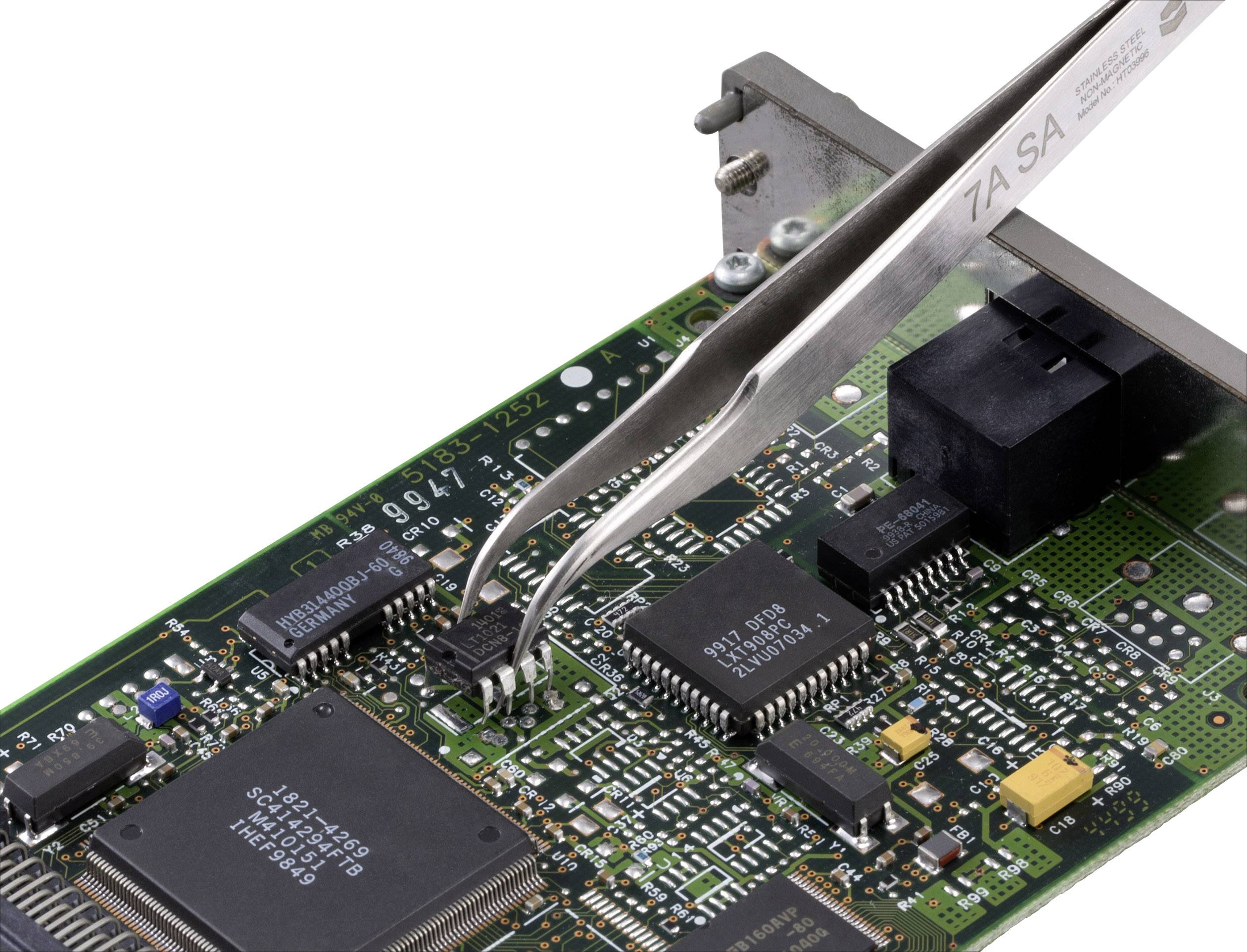 A circuit board with electronic components, including microchips and capacitors. A pair of tweezers is moving a small chip.