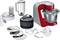 Kitchen mixer in red with various attachments: blender, whisk, dough hook, grating and slicing discs, accessory container.