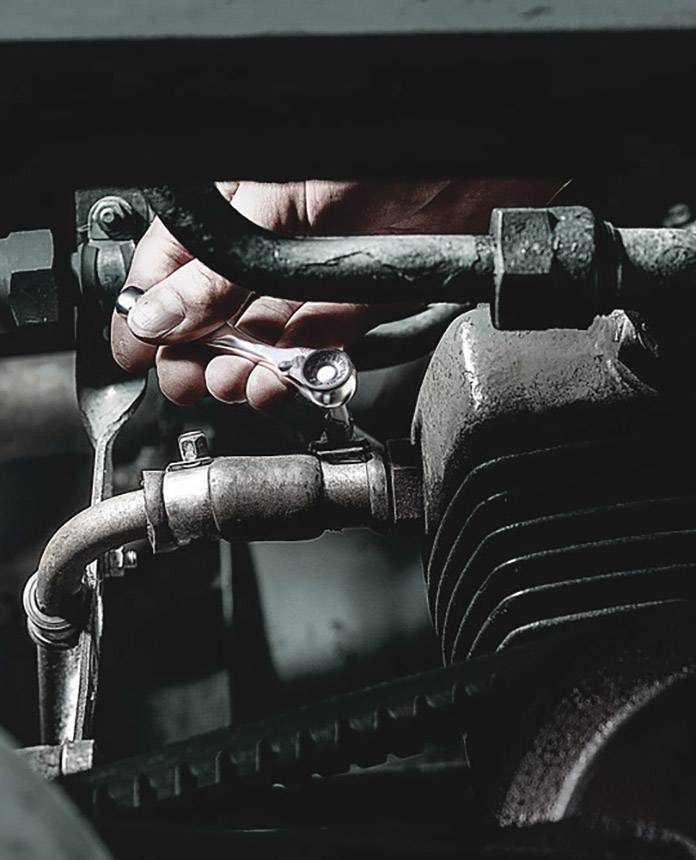 A hand tightens a screw on a motor using a spanner. This is a maintenance or repair task.