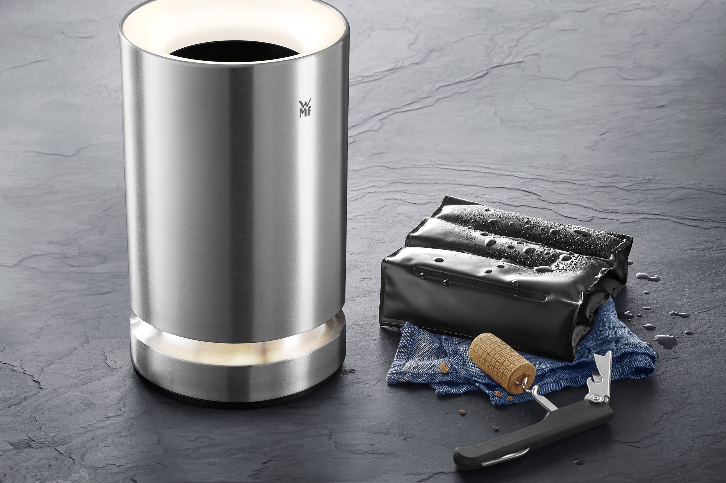 A stainless steel electric bottle cooler next to an opened bottle cap on a blue cloth.