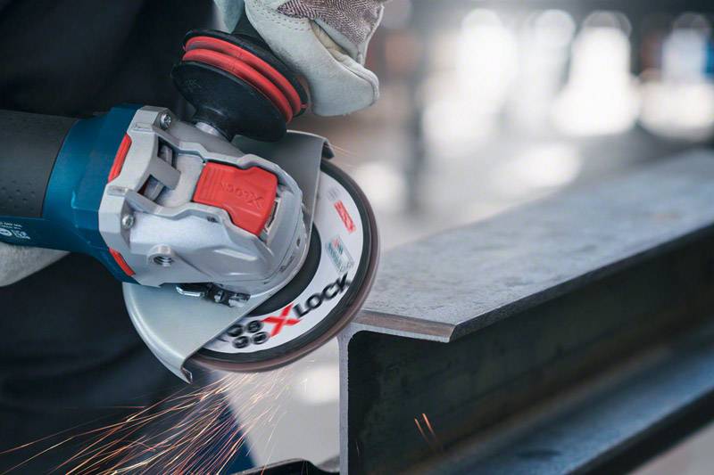 A person is grinding metal with an angle grinder. Sparks are flying from the point of contact, indicating active processing.