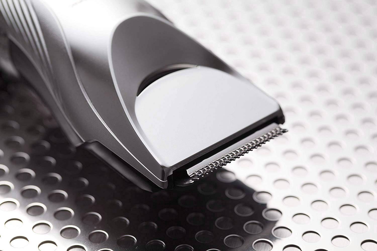 Electric hair clipper with silver casing, resting on a metallic surface.