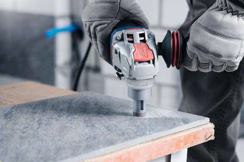 A person wearing gloves is drilling a hole in a grey stone slab using an electric drill.