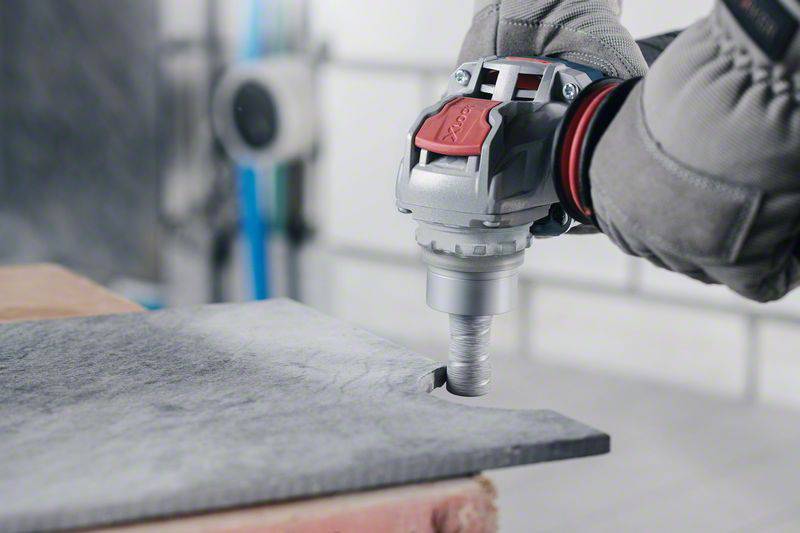 A hand in a work glove holds an electric tool and cuts a piece of metal with precision. Workplace in the background.