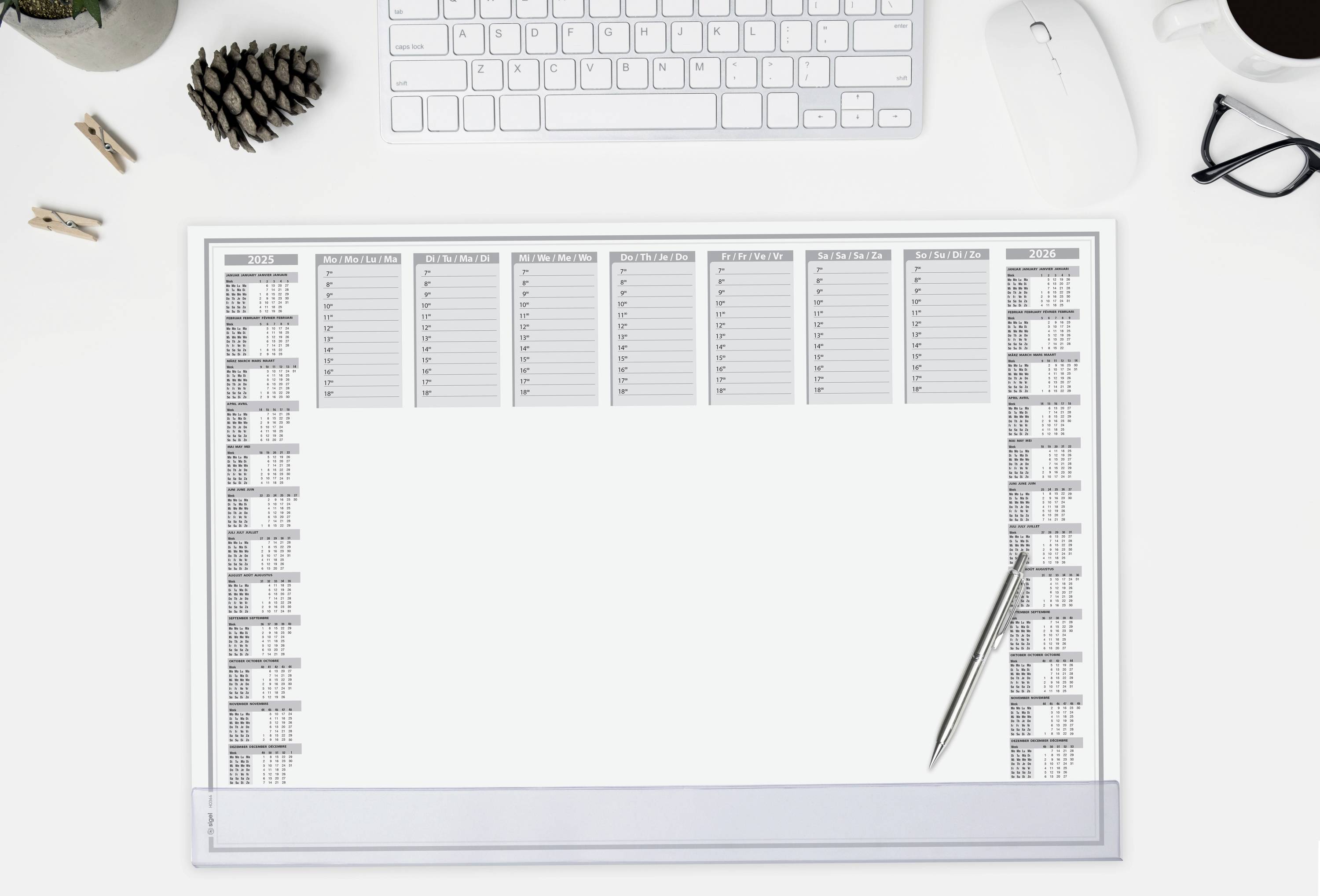 A desk with a keyboard, mouse, glasses, coffee mug and desk calendar. The calendar is blank and lies centrally.
