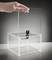 A hand places a clear acrylic lid onto a transparent box with a lock, suggesting security or safeguarding contents.