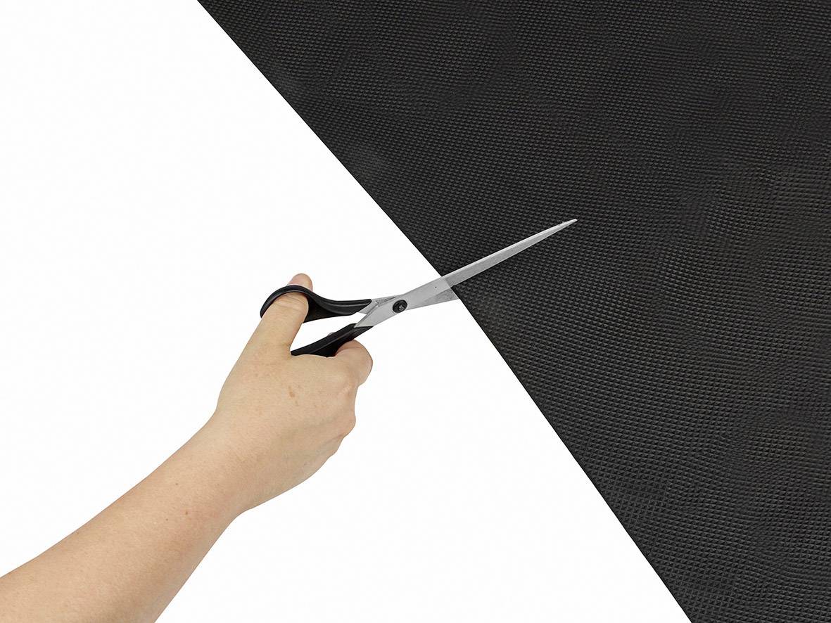 A hand cuts a large, black mesh material along a straight line with a pair of scissors.