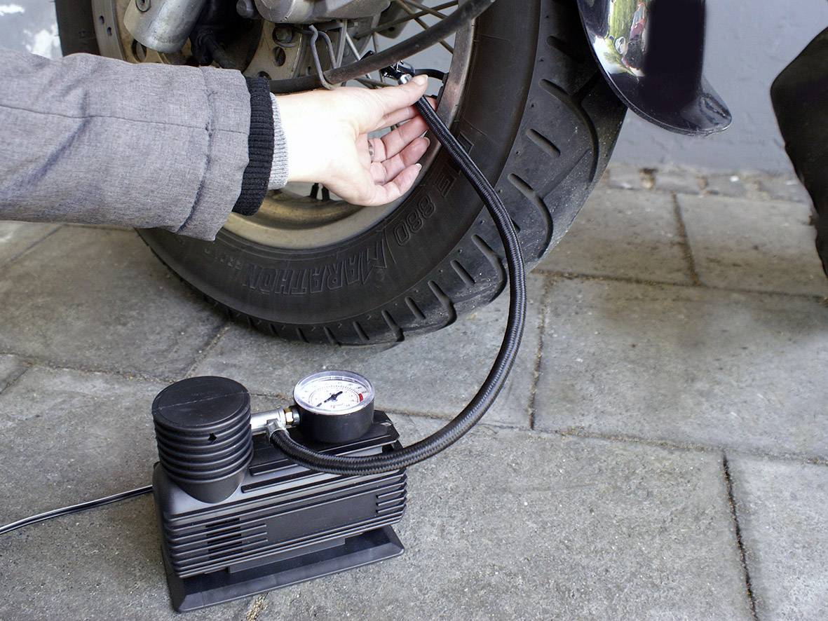 A person is inflating a motorcycle tyre with a portable compressor. The pressure is being displayed on a pressure gauge.