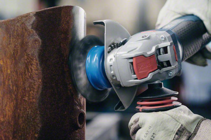 A person wearing protective gloves is holding an angle grinder, grinding a rusty metal surface.