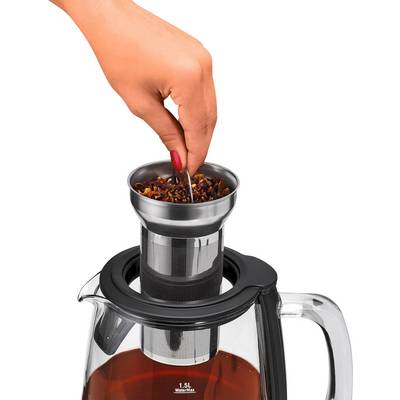 A hand is holding a tea strainer over a glass jug filled with brewed tea.
