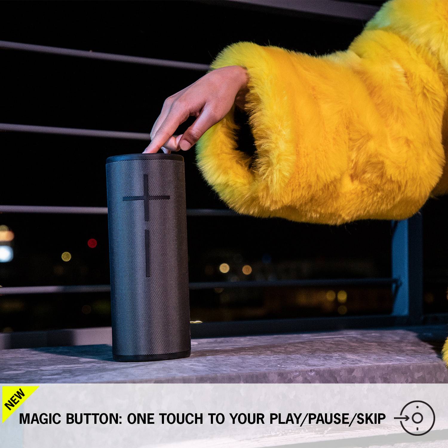 A person wearing a yellow jacket is pressing a button on a black, cylindrical speaker. Text: 'Magic Button: One Step to Music'.