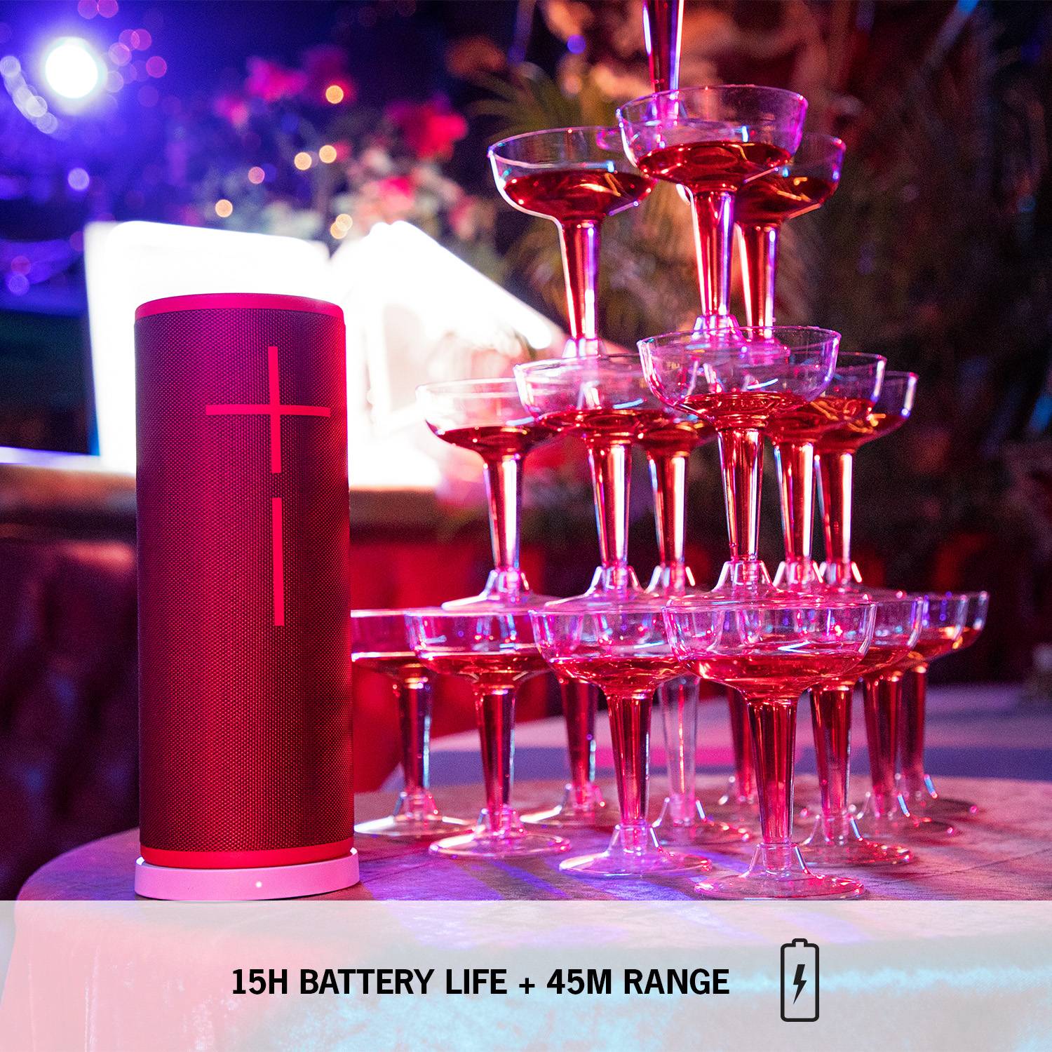 Red portable speaker on a table next to a pyramid of champagne glasses. Text in image: '15h Battery Life + 45m Range'.