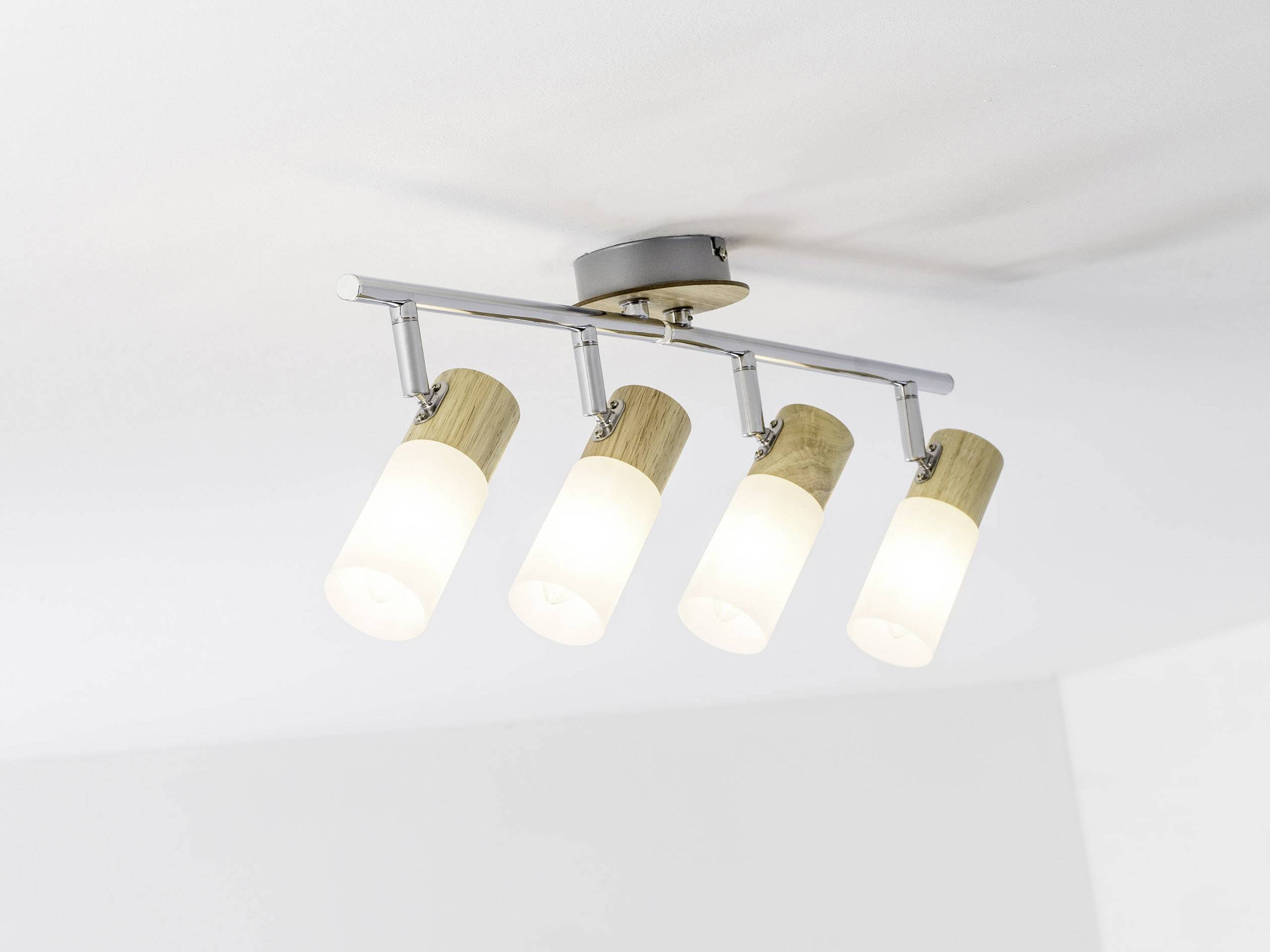 Four cylindrical ceiling lights made of wood and metal, mounted on a metal rod, shine brightly against a white ceiling.