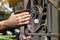 A person is sanding a rusty metal gate railing with sandpaper. Late summer daylight in the background.