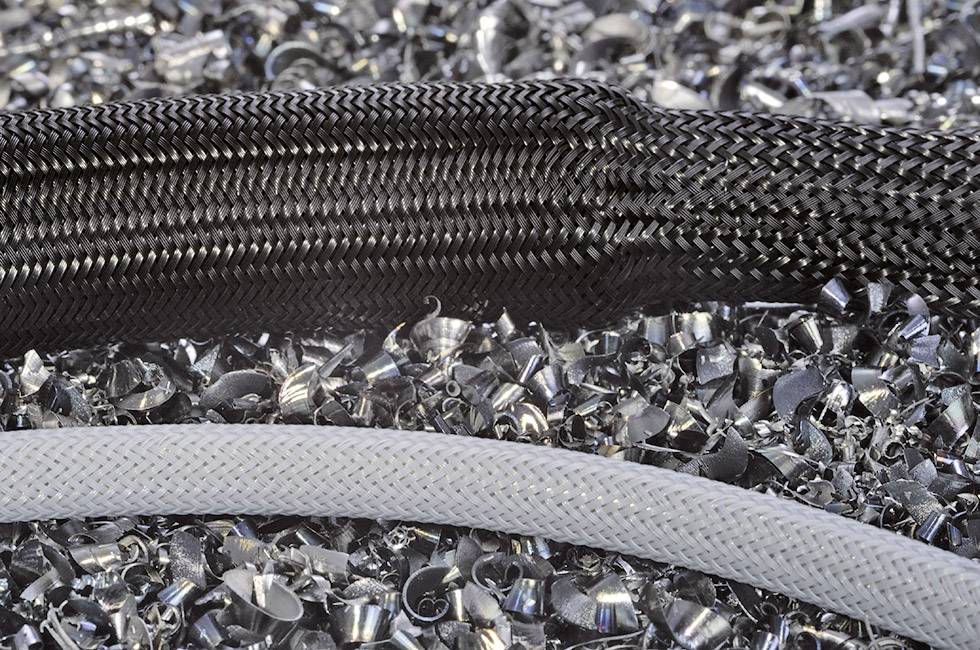 A black and a grey braided cable lie on a pile of metallic shavings.
