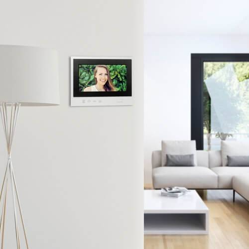 Living room with a grey sofa and coffee table. On the wall hangs a digital photo frame with an image of a smiling person against a green background.