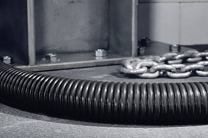 A coiled black cable protection sleeve lies beside a heavy metal chain on a grey floor, with a metal structure in the background.