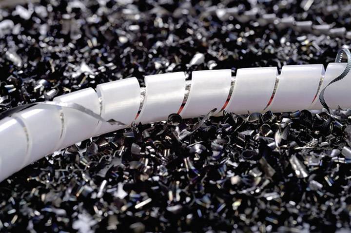 A white plastic tube lies on a pile of black plastic shavings. The focus is on the texture and contrasts of the materials.