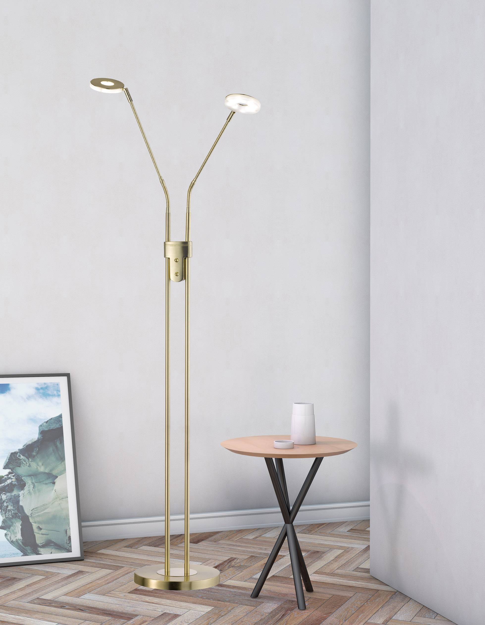 Floor lamp with two illuminating heads stands in a corner next to a small table with a vase. Artwork leans against the wall.