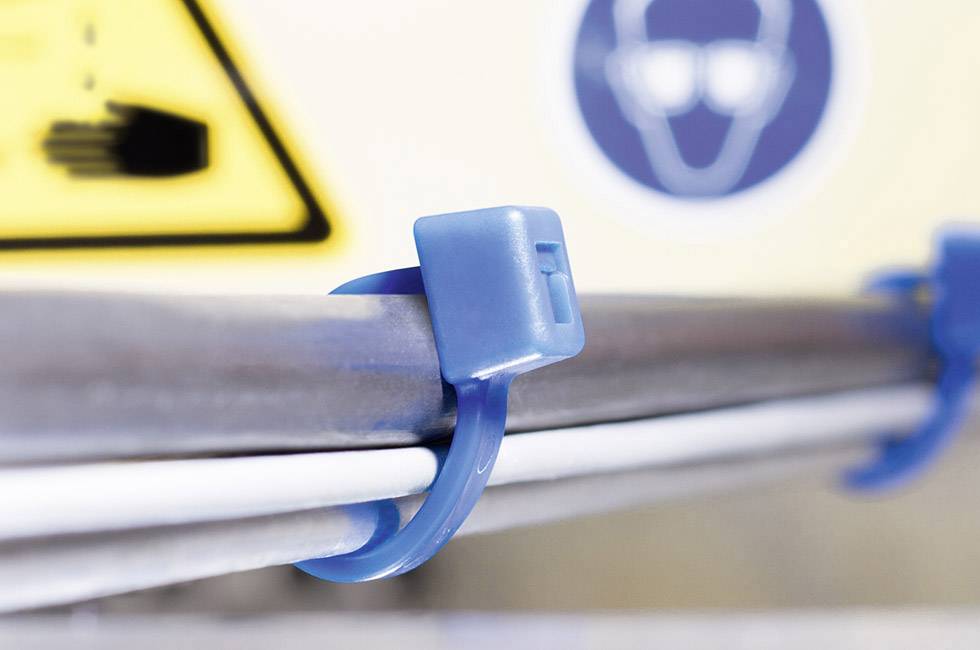 Close-up of a blue cable tie securing multiple cables to a pole. A blurred warning sign is visible in the background.