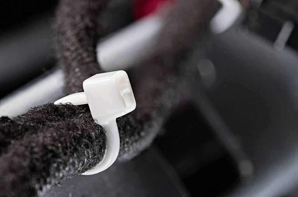 Close-up of a white cable tie holding together a thick black cable bundle. Blurred technical equipment in the background.