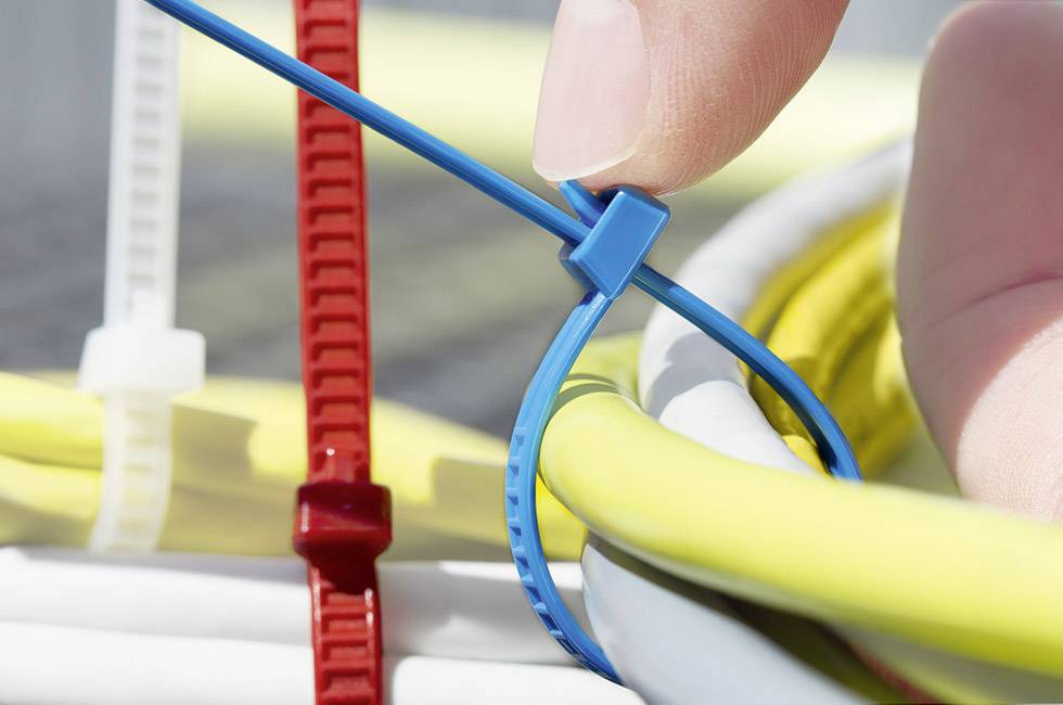 A hand is tightening a blue cable tie to organise yellow cables. Beside it are red and white cable ties.