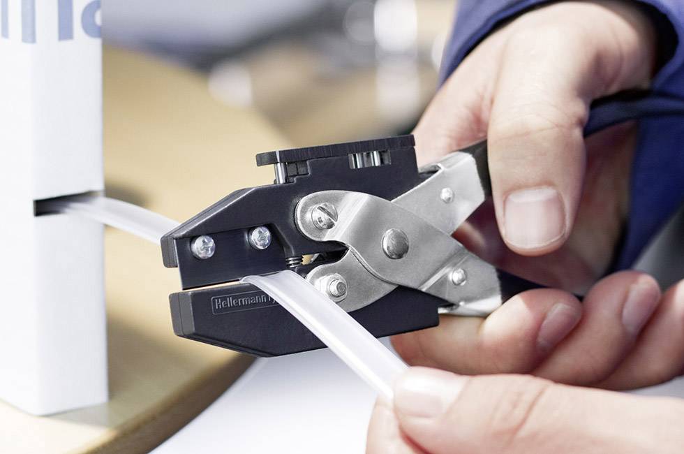 A hand is using a crimping plier to secure a cable to a table.