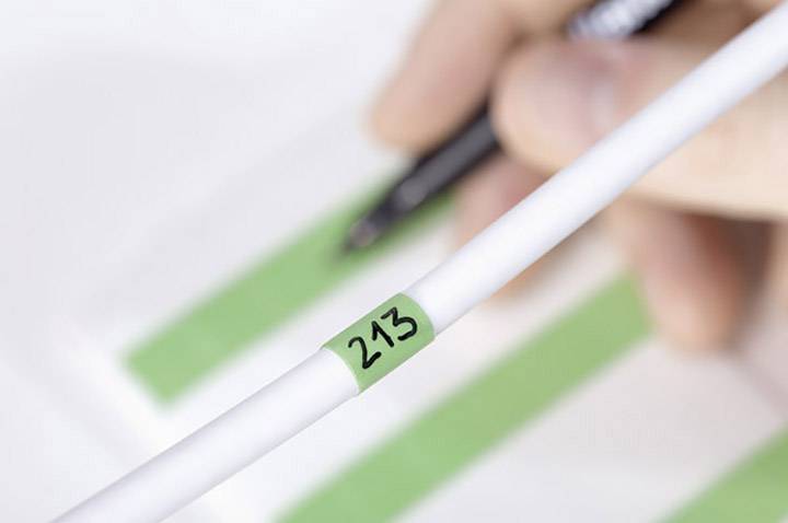A hand is holding a pen over a document with green markings. In the foreground, a cable with the number '213' is visible.