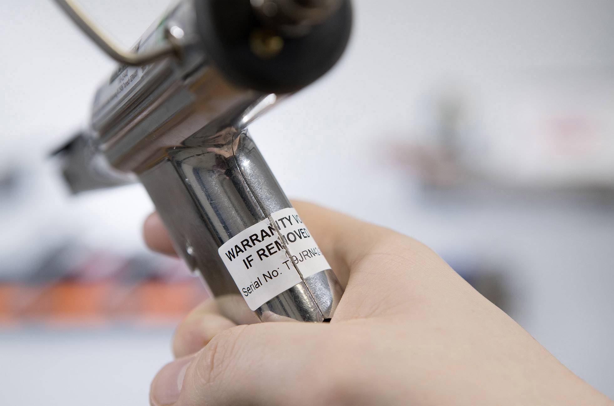 A person is holding a metallic device with a sticker that reads 'WARRANTY IF REMOVED'.