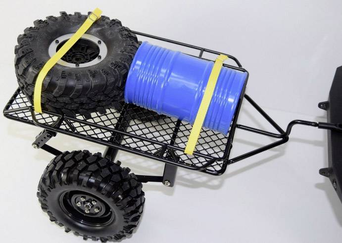 A small hand trolley with chunky tyres is transporting two large, yellow straps that are securing a blue barrel and a black wheel.
