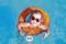 A smiling little girl with heart-shaped sunglasses swims in the blue pool on an orange rubber ring.