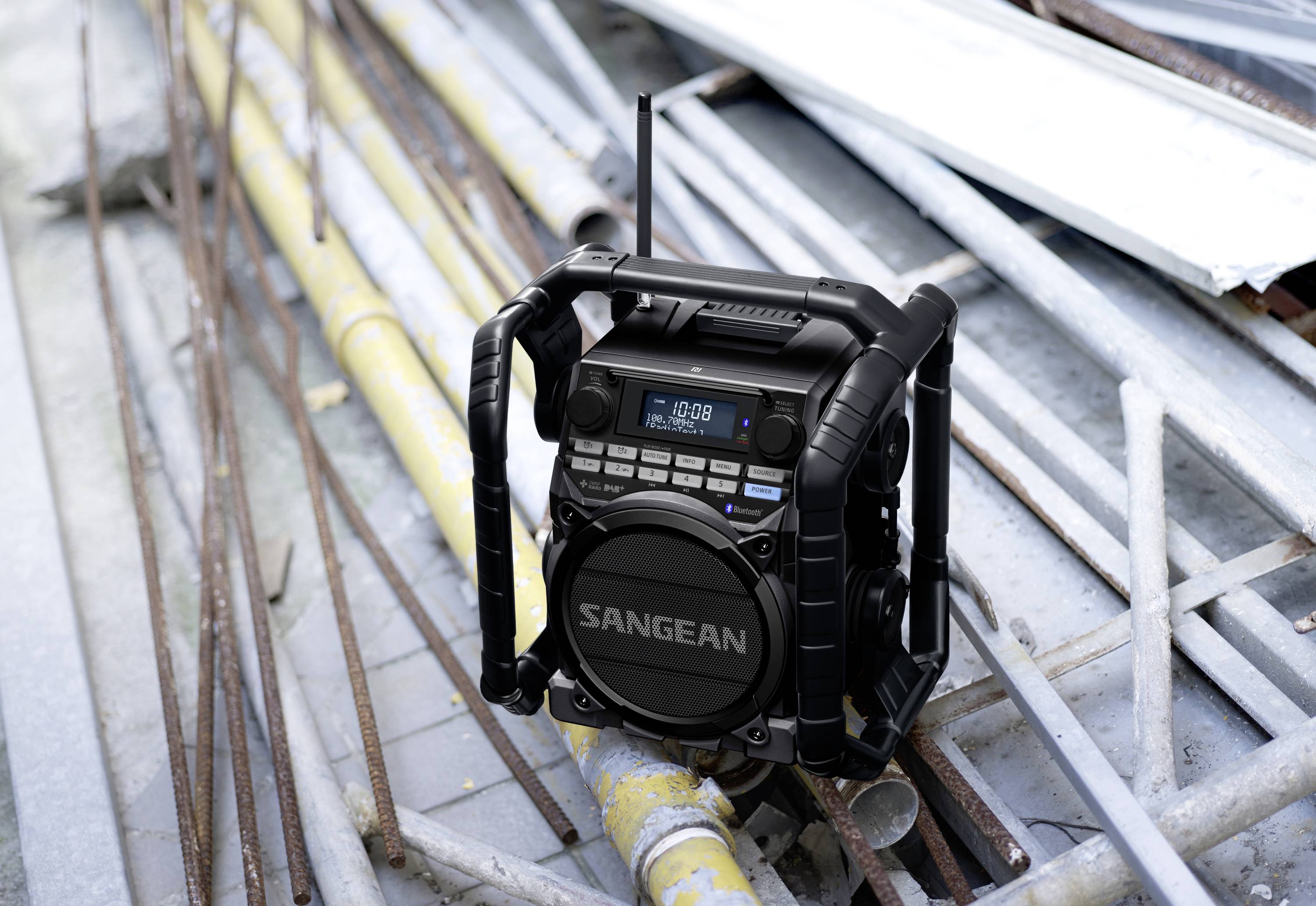 A portable radio with a robust design sits on a stack of scaffolding. The display shows '108.0 MHz', surrounded by metal poles.