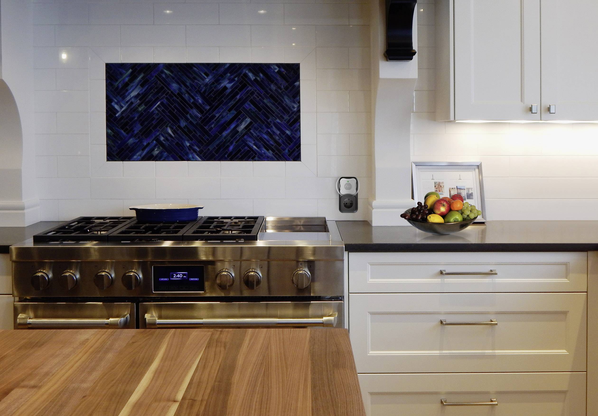 A modern kitchen with a cooker, a wooden worktop and white cupboards. A fruit bowl sits on the counter.