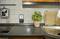 A kitchen with a basil plant pot on the worktop. Beside it are chopping boards and a plug socket.