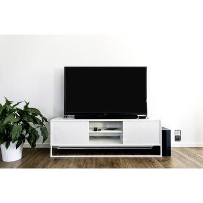 A living room with a large television on a white TV unit. To the left is a green plant, and to the right is a small speaker.