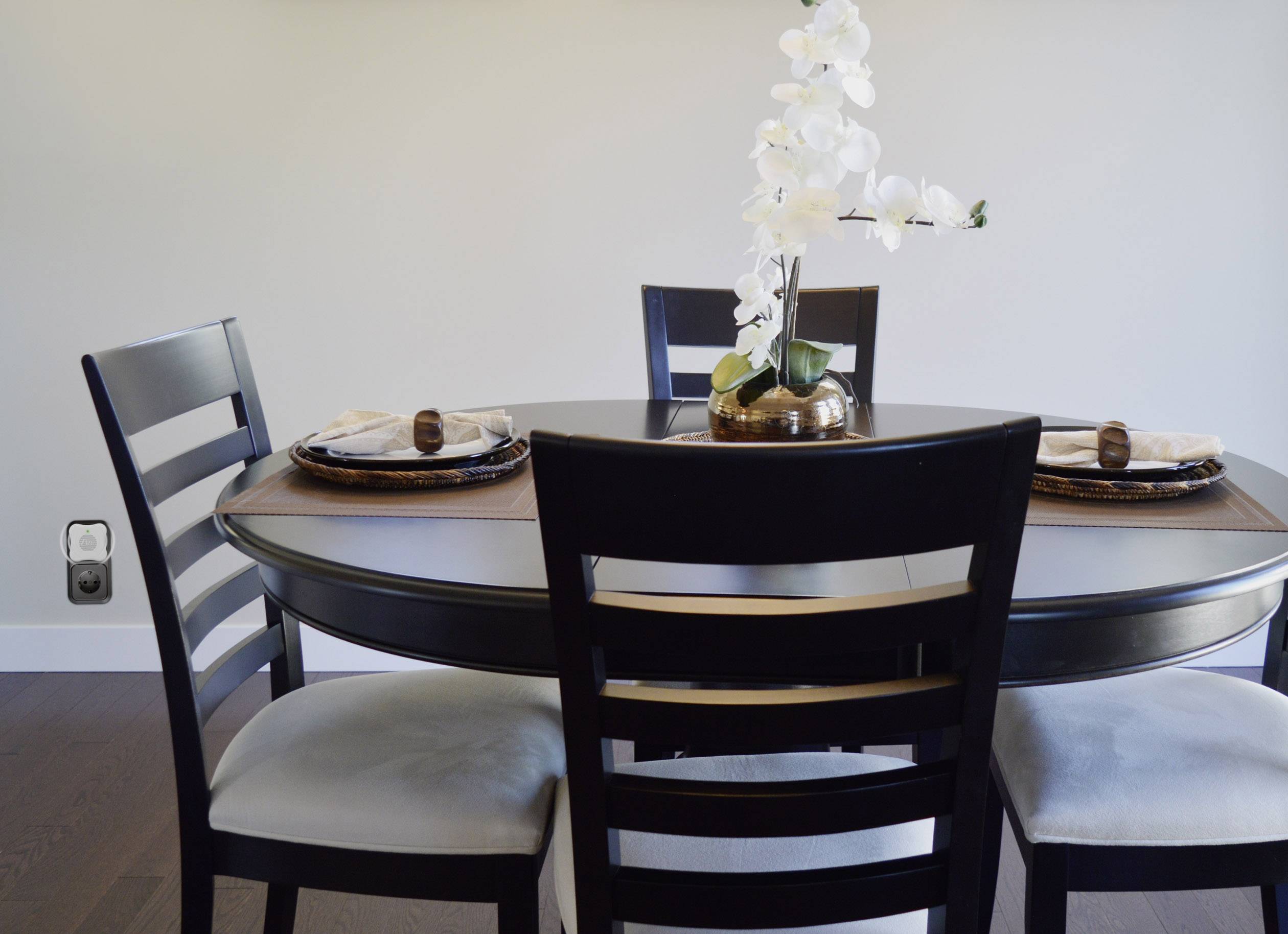 A round dining table with four chairs. A vase with white orchids sits in the centre. The room appears modern and tidy.