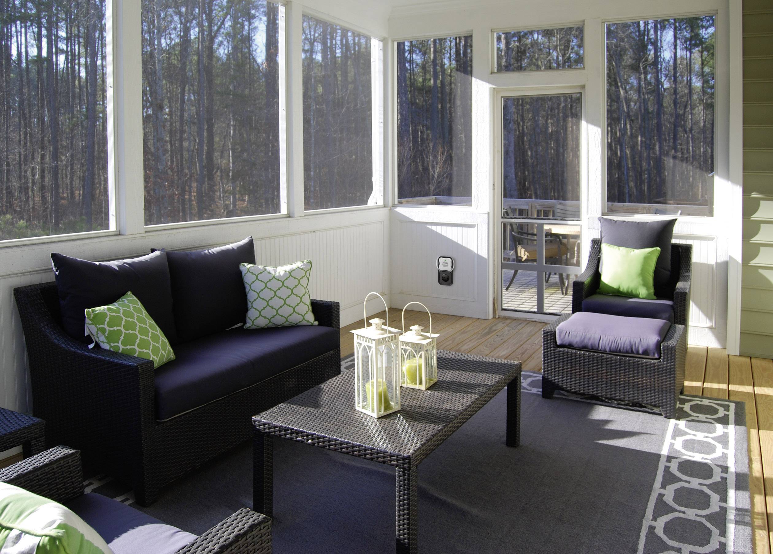 A cosy, covered terrace area with rattan furniture, cushions in green and black, and two decorative lanterns on the table.