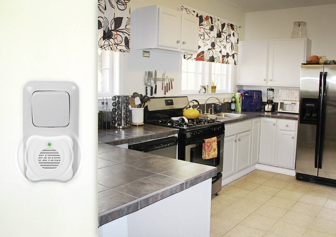 A modern kitchen with white cabinets and stainless steel appliances. A smoke detector is mounted on the wall in the foreground.