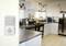 A modern kitchen with white cabinets and stainless steel appliances. A smoke detector is mounted on the wall in the foreground.